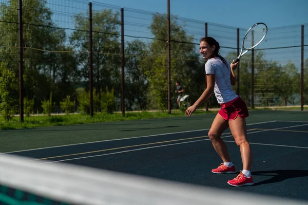 Mladá běloška hraje tenis na venkovním kurtu v horkém letním dni. — Stock fotografie