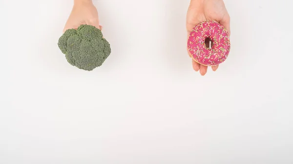 饮食习惯的比较。拿着花椰菜和甜甜圈的女人，背景是白色的 — 图库照片