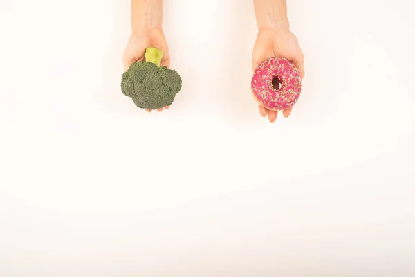 饮食习惯的比较。女人拿着花椰菜和甜甜圈的白色背景。复制空间 — 图库照片