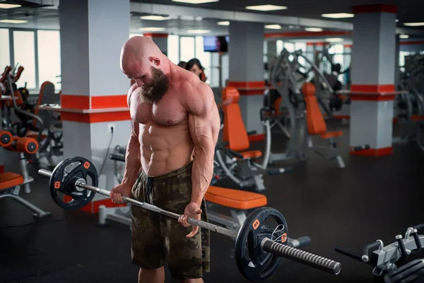 En skallig man med skägg i gymmet. Muskulös bodybuilder kille som gör skivstångsövningar. Stark man med en naken bål. Den unga idrottaren förbereder sig för tyngdlyftningstävlingar. — Stockfoto