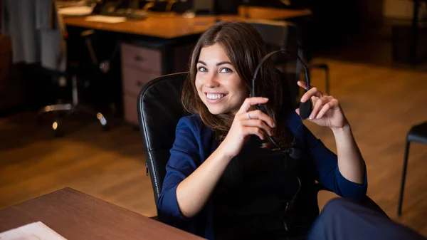 Attraktive Kaukasierin sitzt mit Headset in der Hand am Arbeitstisch im Büro. — Stockfoto