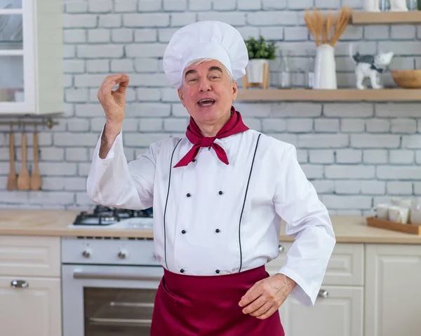 A férfi séf finom gesztust mutat. Idős férfi szakács a konyhában egy étteremben. — Stock Fotó