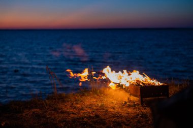 Gün batımında deniz kıyısında şenlik ateşinde bir turist çadırından manzara