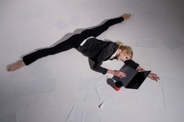 İş elbisesi giymiş bir balerin orta sicimle oturur, dizüstü bilgisayarda çalışır ve kahve içer. Bilgisayar başında esnek bir kadın çalışıyor.