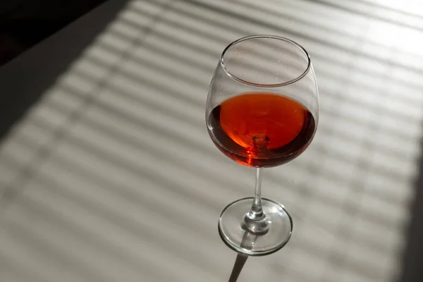Un verre de vin rouge sur une table blanche avec une nuance des stores — Photo