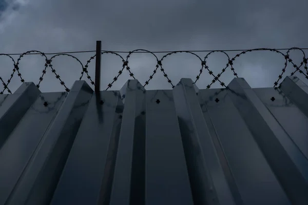 Высокометаллическая гофрированная стена с колючей проволокой и серым небом — стоковое фото