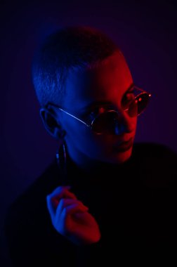 Güneş gözlüklü, kısa saçlı, neon ışıklı güzel bir kadının portresi.