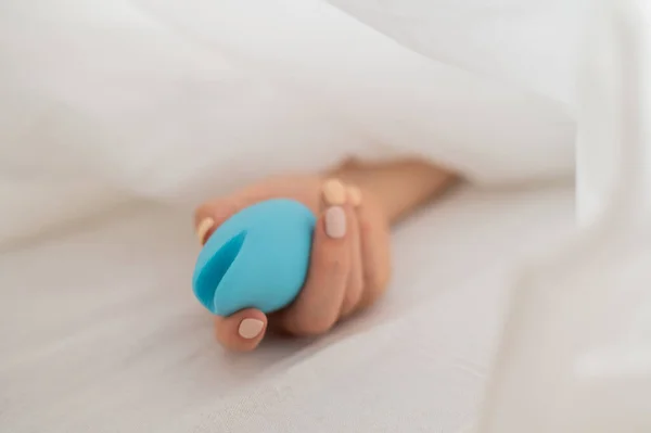 Una donna senza volto giace a letto sotto una coperta con un vibratore clitorideo. La ragazza si masturba — Foto Stock