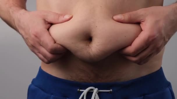 Крупный план мужского жирового трясущегося живота на белом фоне. Толстяк прикасается к животу и показывает большой палец. — стоковое видео