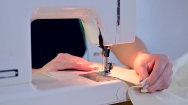 Yakın plan. Bir kadın evde elektrikli dikiş makinesinde çalışıyor.