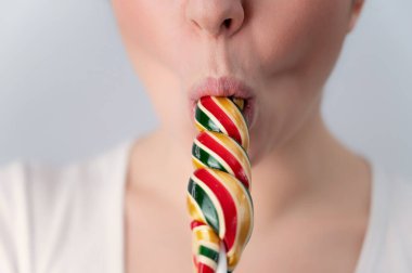 Close-up portrait of a woman sucking a long lollipop against a white background. Blowjob simulation