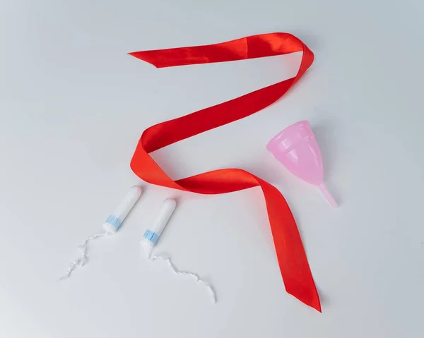Tampon, rosa Menstruationstasse und rotes Satinband auf weißem Hintergrund. Mittel der Intimhygiene einer Frau während der Mentruation — Stockfoto