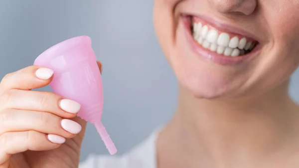 Close-up retrato de mulher branca sorridente segurando copo menstrual rosa no fundo branco. Alternativa para tampões e almofadas em dias críticos. — Fotografia de Stock