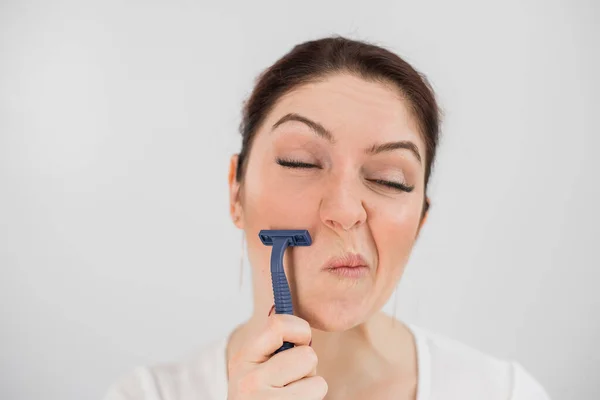 Caucasian funny woman shaves her face with a straight razor on a white background. Copy space. — Stock Photo, Image