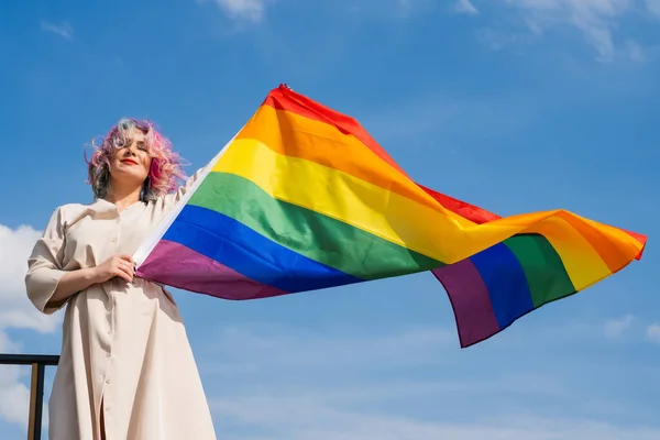 Mujer caucásica con cabello rizado con bandera lgbt. Mujer lesbiana sosteniendo una bandera de arco iris al aire libre —  Fotos de Stock