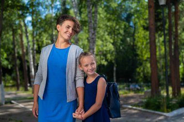 Kısa saçlı, beyaz bir kadın, kızını, bir liseli kızı, elinden tutuyor.