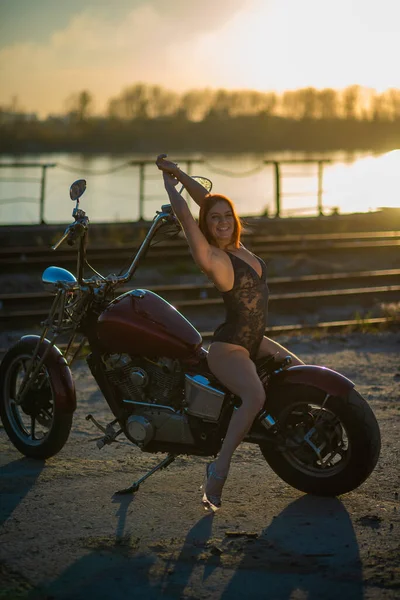 Mujer pelirroja en lencería sexy en tacones altos se sienta en una motocicleta. Atractiva chica pelirroja se sienta en una motocicleta al atardecer —  Fotos de Stock