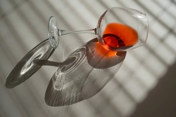 Un verre de vin rouge se trouve sur le côté sur une table blanche avec une nuance des stores — Photo