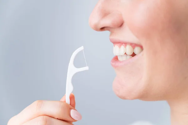 Mulher branca escovando dentes com palito com fio dental no fundo branco. — Fotografia de Stock
