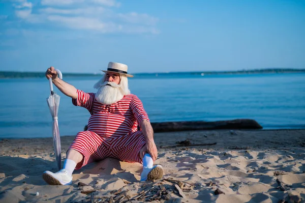 Un vecchio in costume da bagno classico cammina lungo la spiaggia con un ombrellone in una calda giornata estiva — Foto Stock
