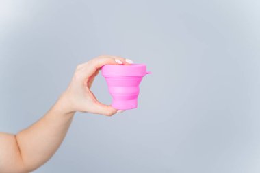 Beyaz arka planda adet bardağını sterilize etmek için plastik bardak tutan kadın. Temizlik için uygun bir konteynır