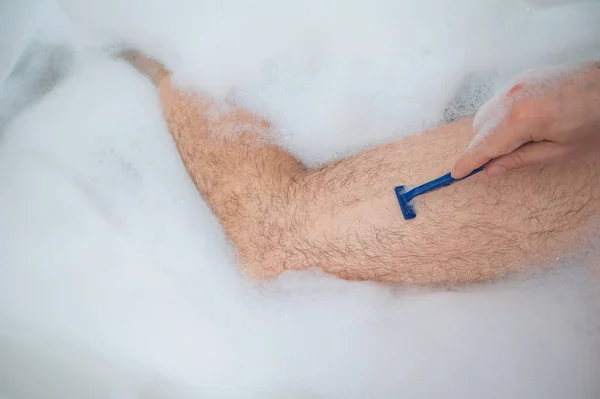 Αστεία φωτογραφία ενός άντρα να κάνει ένα χαλαρωτικό μπάνιο και να ξυρίζει τα πόδια του. Κοντινό πλάνο αρσενικών ποδιών σε αφρόλουτρο. Άνω όψη. — Φωτογραφία Αρχείου