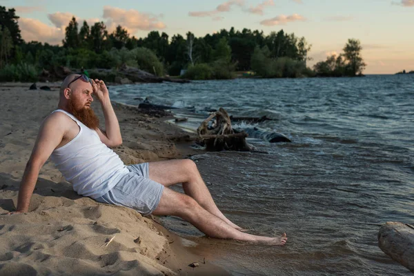 Divertente uomo calvo con la barba rossa vestita in biancheria intima in posa sulla spiaggia. Una parodia maschile divertente di una ragazza glamour. — Foto Stock