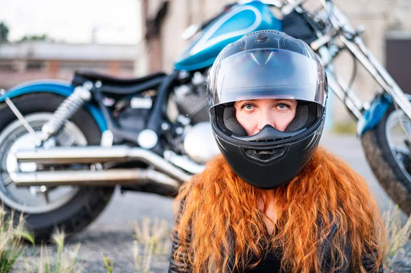 Mulher encaracolada ruiva em um capacete perto de uma motocicleta. — Fotografia de Stock