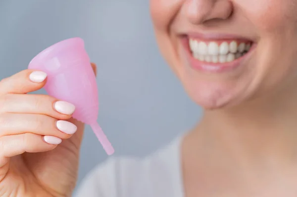 Retrato de cerca de una mujer caucásica sonriente sosteniendo una copa menstrual rosa sobre fondo blanco. Alternativa a tampones y almohadillas en días críticos. — Foto de Stock