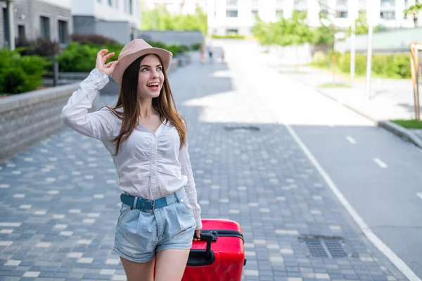 Mooie Kaukasische brunette vrouw in een hoed poseren met een koffer op een stad straat. — Stockfoto