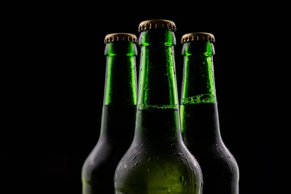 Три бутылки пива из зеленого стекла на черном фоне. — стоковое фото