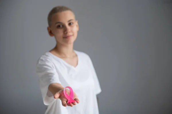 Mujer joven con el pelo corto con una camiseta blanca que sostiene una cinta rosa como símbolo de cáncer de mama sobre un fondo blanco. — Foto de Stock