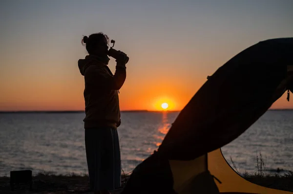 Femme se reposant dans une tente dans la nature au coucher du soleil. La fille s'est installée au bord de la rivière. — Photo