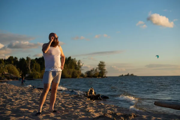 Ett humoristiskt porträtt av en brutal man i t-shirt och boxare på stranden vid solnedgången — Stockfoto