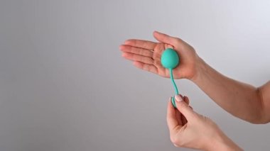 Yüzü olmayan kadın vajinal bir top gösteriyor. Kız, beyaz arka planda pelvik zemin kaslarını çalıştırmak için bir kegel antrenörünü eliyle sıkıyor..