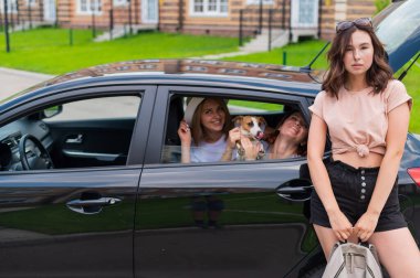 Mutlu üç kadın arabada oynaşıyor. Kız arkadaşlar köpekle araba ile seyahat ederler.
