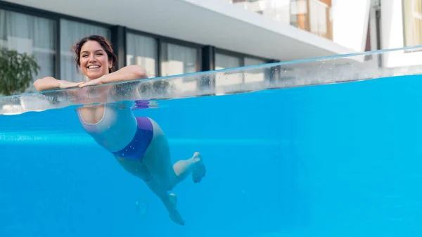 Mujer caucásica feliz nada en una piscina al aire libre con una pared transparente en un hotel —  Fotos de Stock