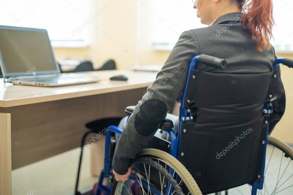 Young woman works at a laptop while sitting in a wheelchair in a university lecture hall. Conditions for teaching a disabled person