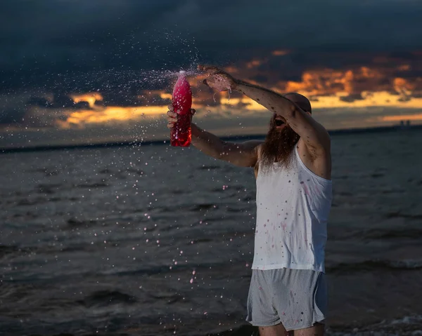 Un ritratto umoristico di un uomo brutale che versa soda da una bottiglia sulla spiaggia al tramonto — Foto Stock
