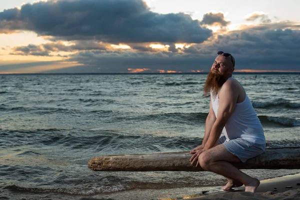 Divertente uomo calvo con la barba rossa in posa sulla spiaggia al tramonto. Una parodia maschile divertente di una ragazza glamour. — Foto Stock