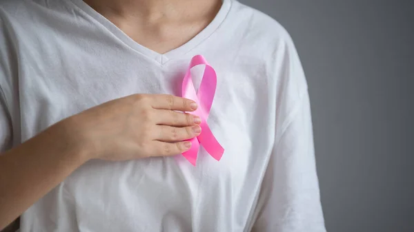 Uma mulher sem rosto usando uma camiseta branca segura uma fita rosa como um símbolo de câncer de mama em um fundo branco. — Fotografia de Stock