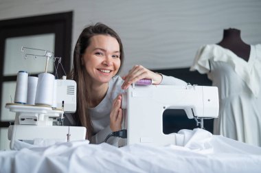 Genç beyaz kadın evde dikiş dikiyor.