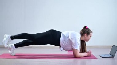 Tombul genç bir kadın tahtada durur ve bir dizüstü bilgisayardan spor dersi izler. Uzaklık sporları eğitimi.