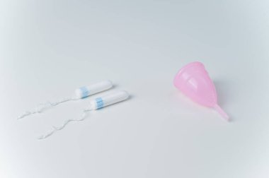 Pembe regl kupası ve beyaz arka planda tamponlar. Regl döneminde kadınlar için kişisel hijyen ürünlerinin karşılaştırılması