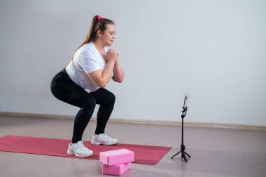 Tombul genç bir kadın bir cep telefonundan online fitness dersi izliyor. Uzaklık sporları eğitimi