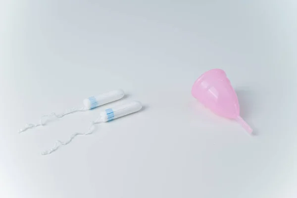 Roze menstruatiecup en tampons op een witte achtergrond. Vergelijking van persoonlijke hygiëneproducten voor vrouwen tijdens de menstruatie — Stockfoto