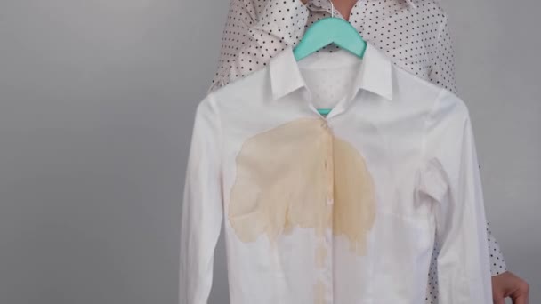 Una mujer compara dos camisas blancas antes y después del lavado. La chica sostiene una blusa, limpia y planchada, y la otra, sucia con manchas de café — Vídeos de Stock