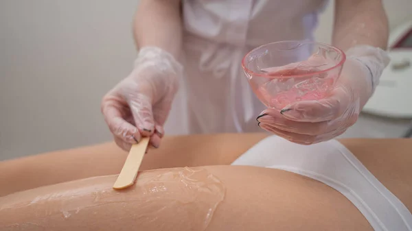 Usta, lazer tüyü çıkarmadan önce kadın bacaklarına spatulayla anestezi jeli uyguluyor. Klinikte bir cihazla kalıcı kılların alınması. — Stok fotoğraf