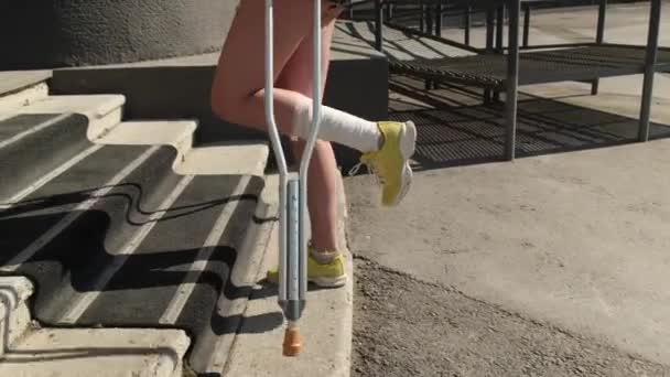 Mujer joven con lesión en el tobillo sube escaleras en muletas. — Vídeos de Stock