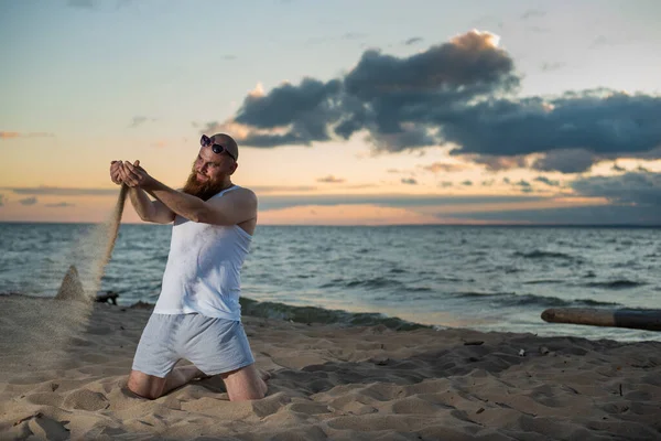 Divertente uomo calvo con la barba rossa in posa sulla spiaggia al tramonto. Una parodia maschile divertente di una ragazza glamour. — Foto Stock